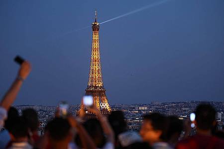 Jan Woitas/dpa | Paris im Sommer 2024 - besonders beliebt: Touristen fotografieren den Eiffelturm mit den Olympischen Ringen von der Terrasse des Triumphbogens. (Archivbild)