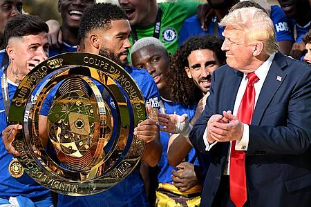 Sven Hoppe/dpa | Chelseas Kapitän Reece James (l/vorn) hält auf dem Siegerpodest die Trophäe in den Händen und schaut irritiert zu US-Präsident Donald Trump.