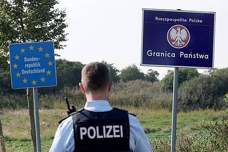 Bernd Wüstneck/dpa | Ein Bundespolizist steht vor den Schildern für Deutschland und Polen. Als Reaktion auf die deutschen Kontrollen will nun auch Polen an der Grenze kontrollieren. (Archivbild)