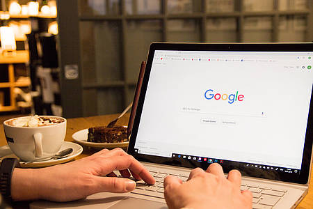 Hände auf Laptoptastatur, Bildschirm vom Laptop zeigt die Suchmaschine Google.com