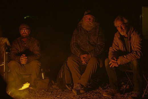 Drei Camper sitzen bei Nacht um ein Lagerfeuer.
