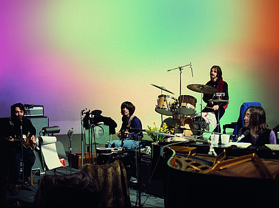 Die Beatles sitzen vor eine farbig beleuchteten Wand.