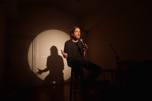 Bo Burnham sitzt im Dunkeln auf einem Stuhl und wird von einem Spotlight angestrahlt.