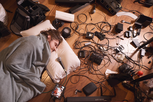 Bo Burnham liegt inmitten von unordentlichem Video-Equipment eingewickelt in eine Decke und spricht in ein Mikrofon.