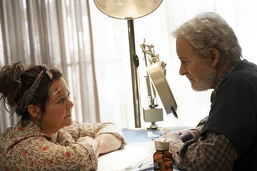 Melissa McCarthy und Kevin Kline sehen sich über einen Tisch hinweg an