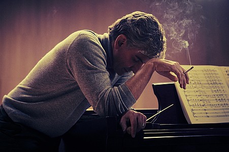 Bradley Cooper als Leonard Bernstein im Netflix-Film Maestro sitzt rauchend am Piano. 