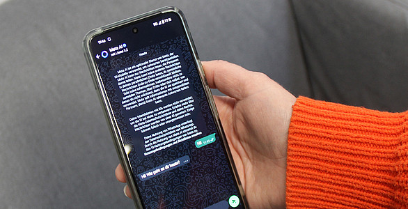 Fran hält Handy mit WhatsApp-Chat mit MetaAI in die Kamera.