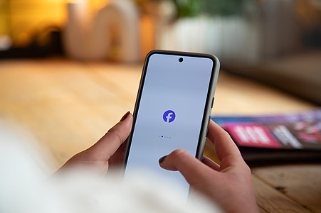 Hände mit Smartphone in der Hand. In der Mitte das Facebook Logo.