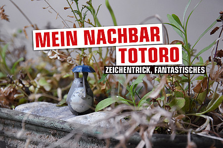 Ein Figur von Totoro steht in einem Beet aus Gräsern