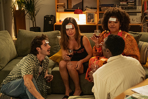 Eine Szene aus "Eine perfekte Geschichte" auf Netflix: Margot und David sitzen mit ihren Freunden im Wohnzimmer und spielen "Wer bin Ich"