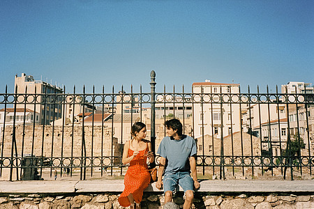 David und Margot, das Paar aus "Eine perfekte Geschichte" auf Netflix, sitzt auf einer Mauer vor blauem Himmel.