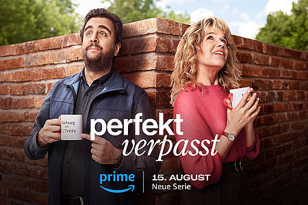 Anke Engelke und Bastian Pastewka lehnen als Hauptcharaktere von Perfekt Verpasst auf Prime Video an einer Mauer.