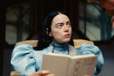Emma Stone im Film "Poor Things" mit einem Buch, schaut zur Seite 