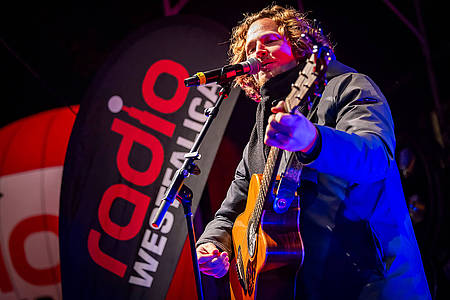 Michael Schulte steht mit seiner Gitarre auf einer Bühne und singt in ein Mikrofon