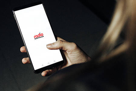 Frau hält Smartphone mit geöffneter Radio Westfalica-App